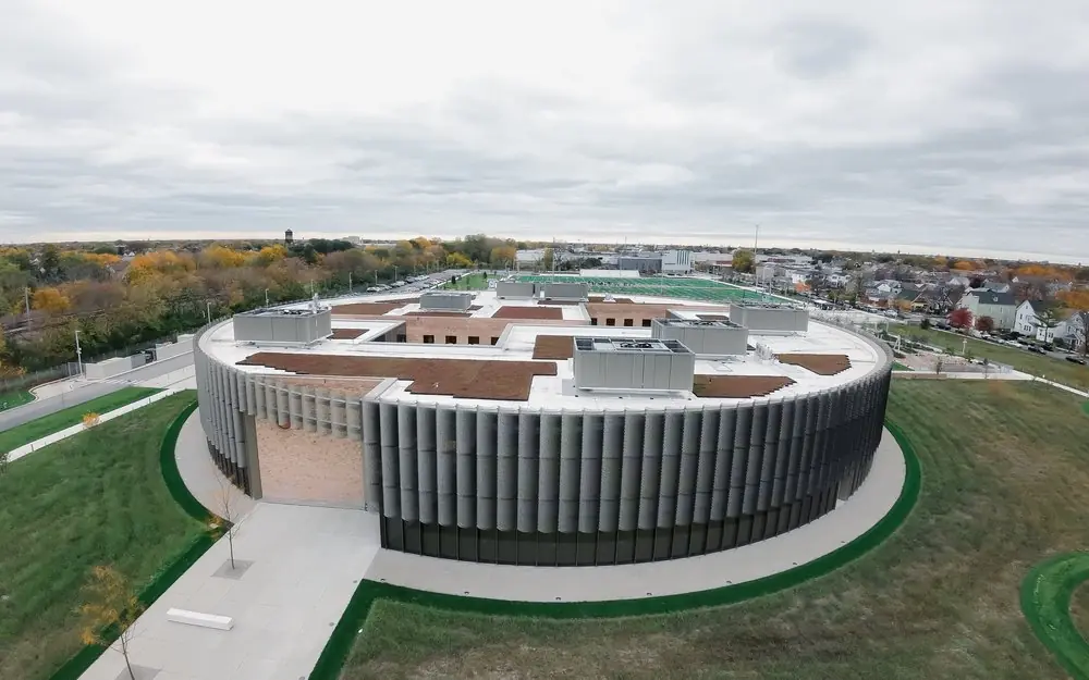 Aerial view of a round, ribbed civic building ringed by lawns under an overcast autumn sky.