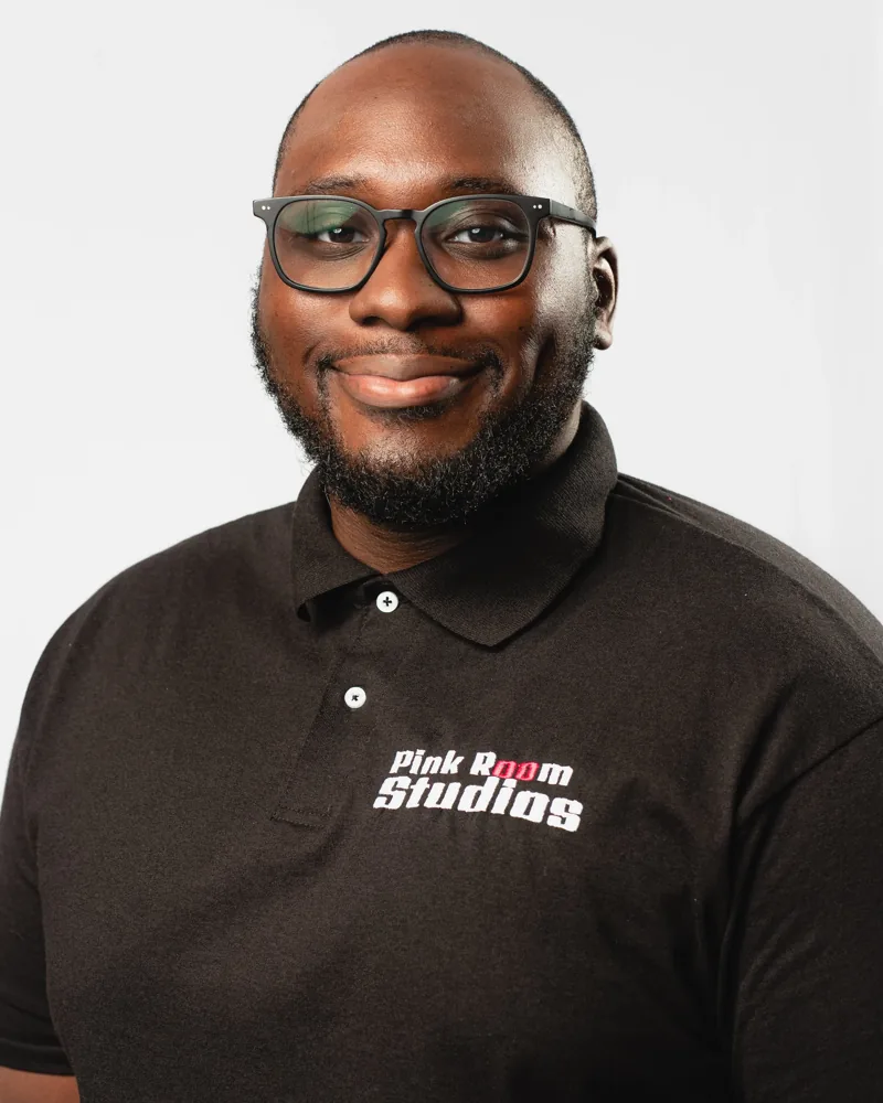 Portrait of Abdul Brimah, smiling, in glasses and a black PinkRoom Studios polo.