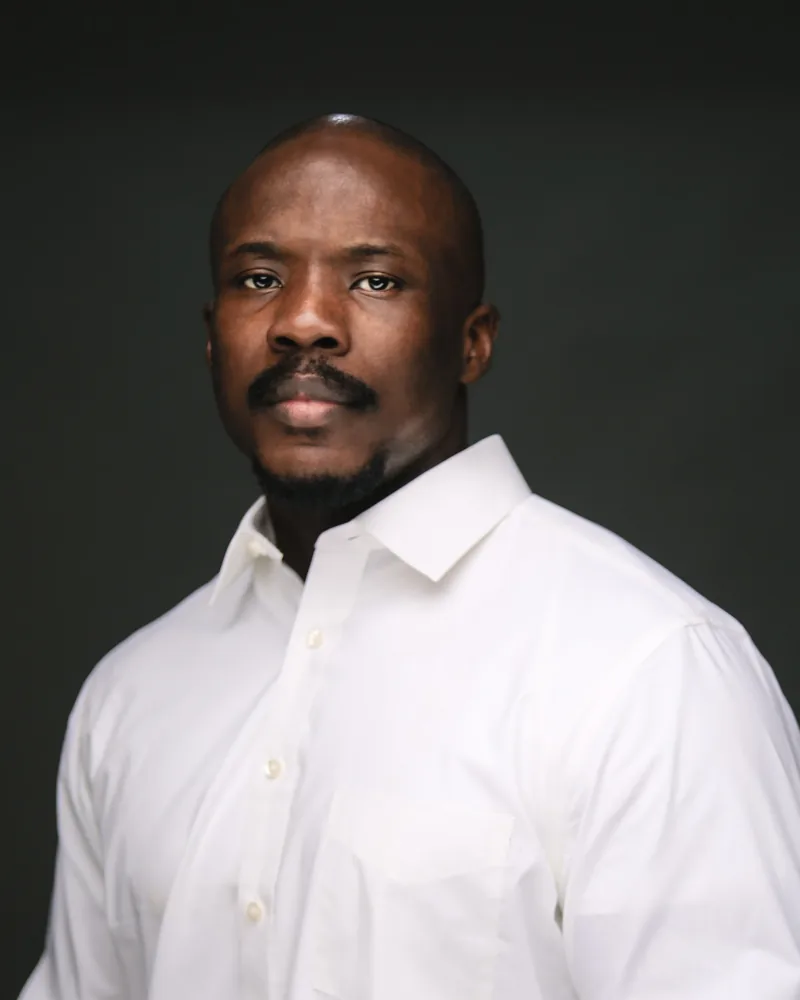 Portrait of Omasan Wyse in a white shirt against a dark backdrop.